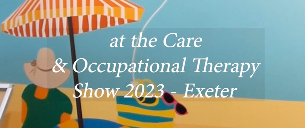 ATADesigns and Wallsmiths Wallpapers stand at the Care and Occupational Therapy Show in Exeter 2023. Image features woman sitting on the beach wearing sun hat and under an umbrella looking out to the sea