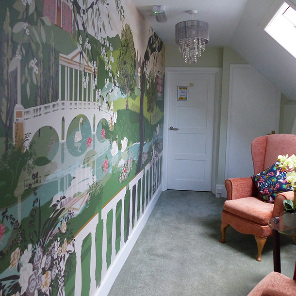 Nature wall mural illustration featuring swans in a lake under a bridge and a stately home on a hill with trees in the foreground in a quiet room at Adamscourt Care Home for Vauxian Care.  Design by ATADesigns.