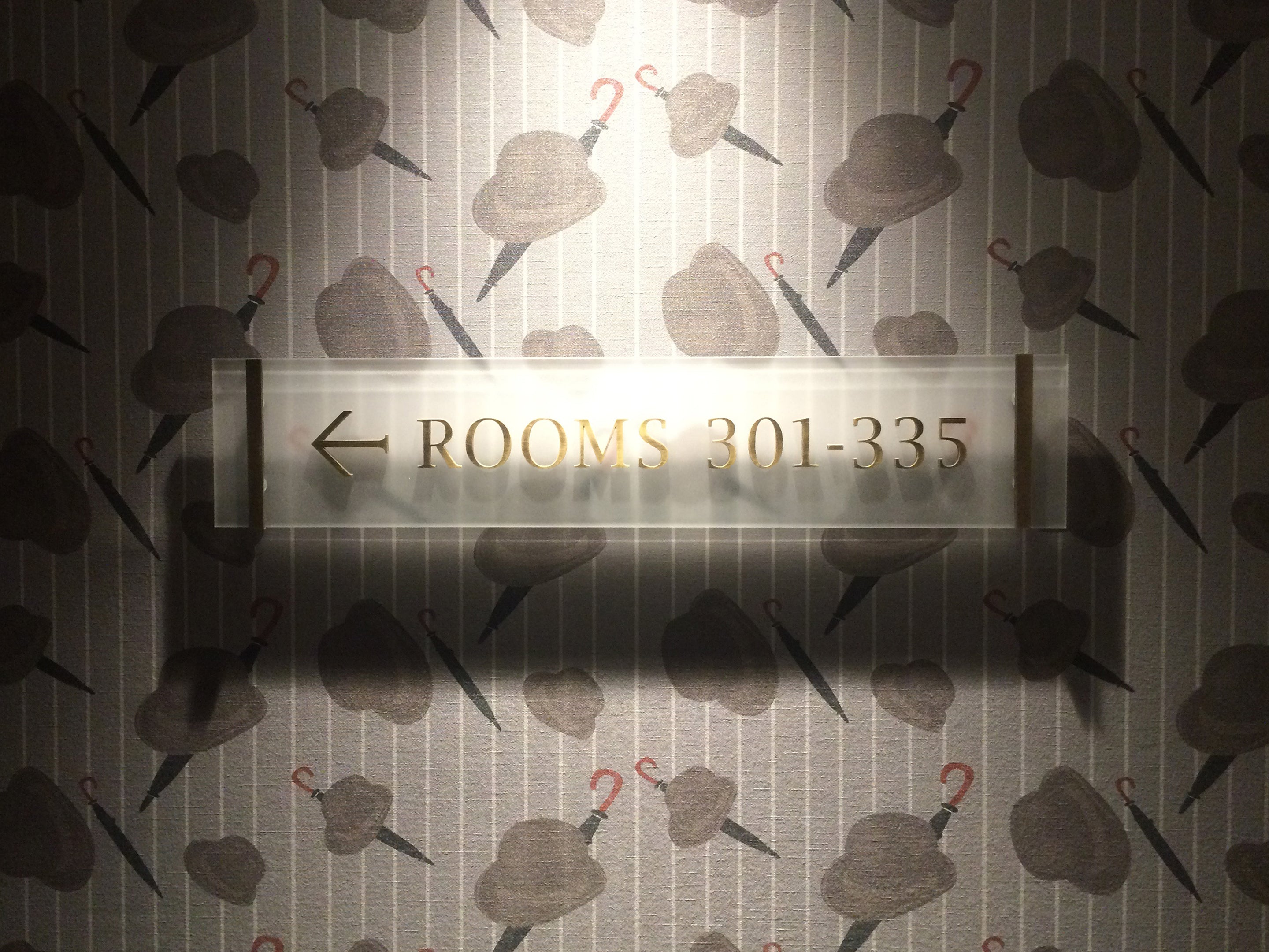 Close up of he Bowler wallpaper design by ATADesigns featuring Bowler hats and Umbrella's in repeat at The London Marriot Hotel.  Room numbers sign is fitted on the wall