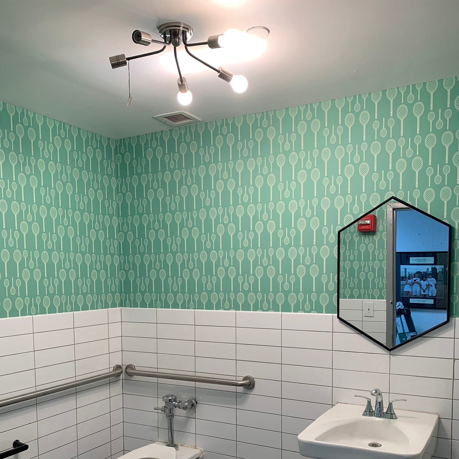 Bathoom with sink, mirror and rail with whit tiles on wall and green tennis wallpaper above tiles.  Tennis wallpaper by ATADesigns