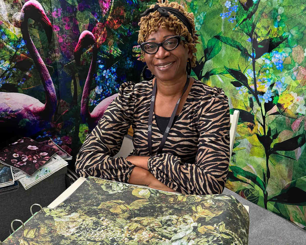 Annette Taylor-Anderson sitting at a table with colorful artwork featuring flamingos and floral designs in the background.