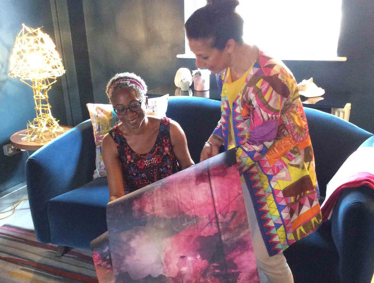Annette Taylor-Anderson of ATADesigns and Elisa Fanella of Elisa Interiors in a room looking at a colorful wallpaper design in a colourful room with blue sofa.  Wallpaper design by ATADesigns.