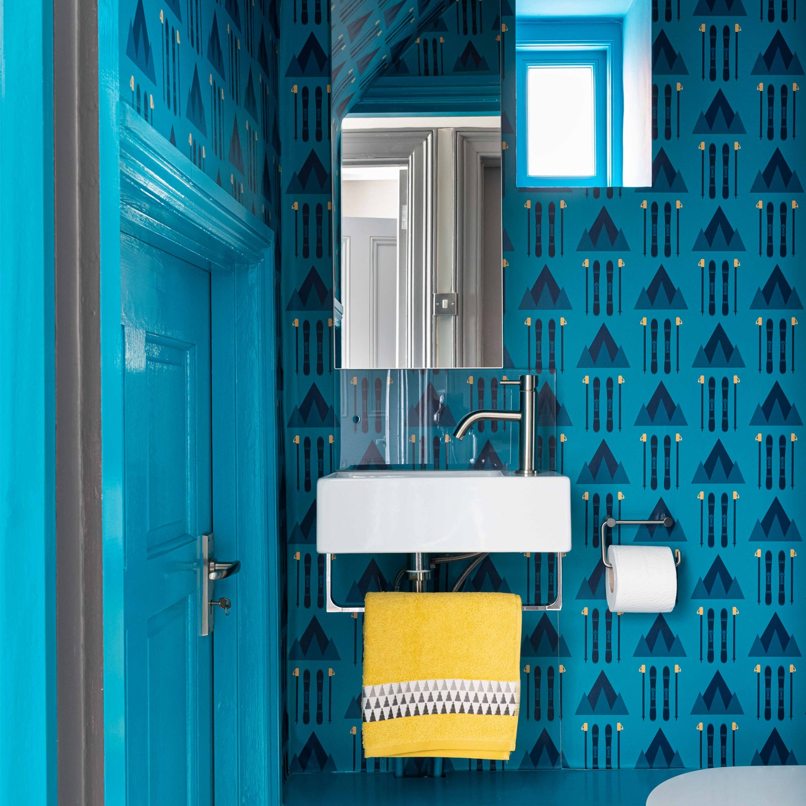Ski Wallpaper Design by ATADesigns in bathroom project by  interior designer Emma Green Design.  This modern bathroom is painted blue, with mirrors and small sink on the wall, and yellow towel hanging from  hand rail.