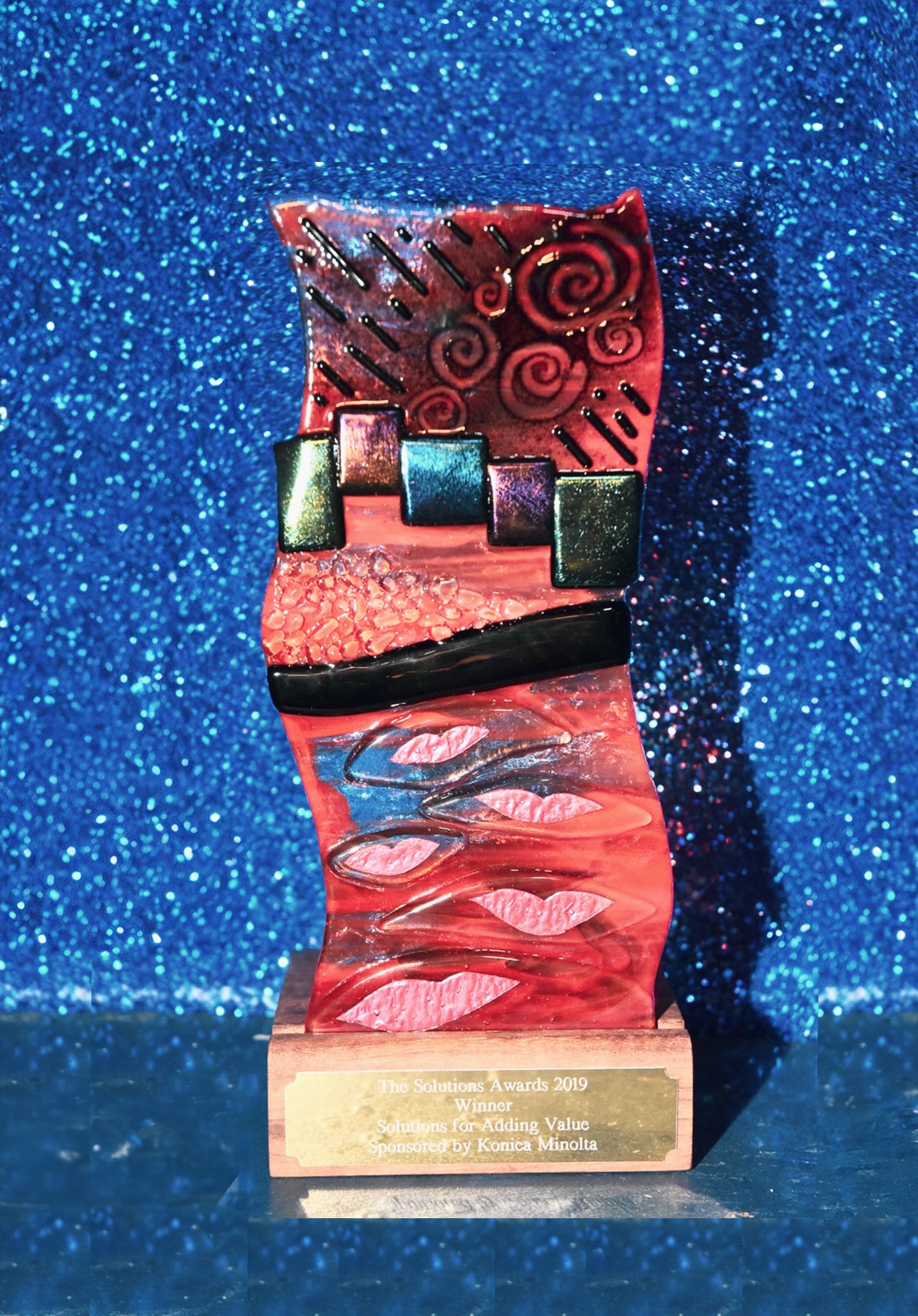 Decorative trophy with red and black, multicoloured design on a glue glittery background for the Print Solutions Awards