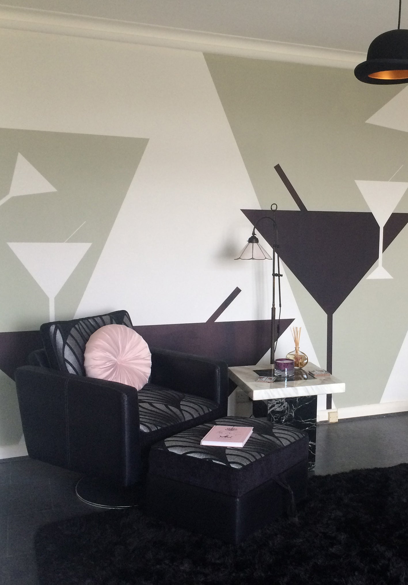 Modern living room with black armchair, ottoman, and decorative 'Tipsy' Art Deco mural design featuring large cocktail glasses by ATADesigns