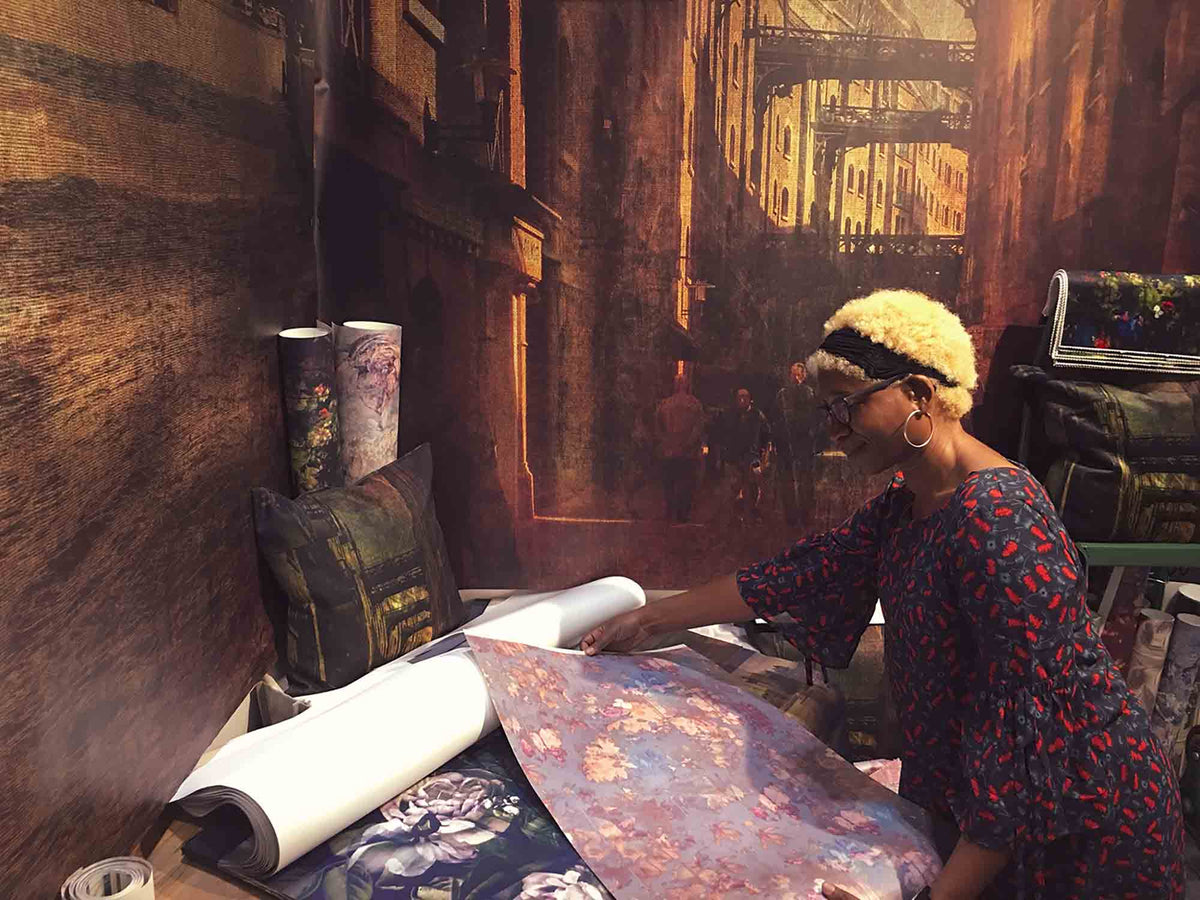 Annette Taylor-Anderson working and looking at wallpaper design with fabric in a studio setting.  Featuring large scale vintage mural designs in setting.  Wallpaper and mural designs by ATADesigns.