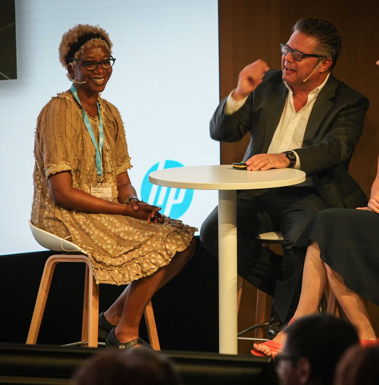 Annette Taylor-Anderson sitting down at table being interviewed on stage by Terry Raghunath at HP Printed Interiors Forum in Barcelona.