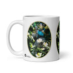 Peacock Glam mug by ATADesigns with a blue peacock, green foliage and white flowers, handle on the left.