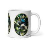 Peacock Glam mug by ATADesigns with a blue peacock, green foliage and white flowers, handle on the right.