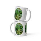 Two stacked Pure Nature mugs by ATADesigns, showing green botanical artwork with birds and blue flowers.