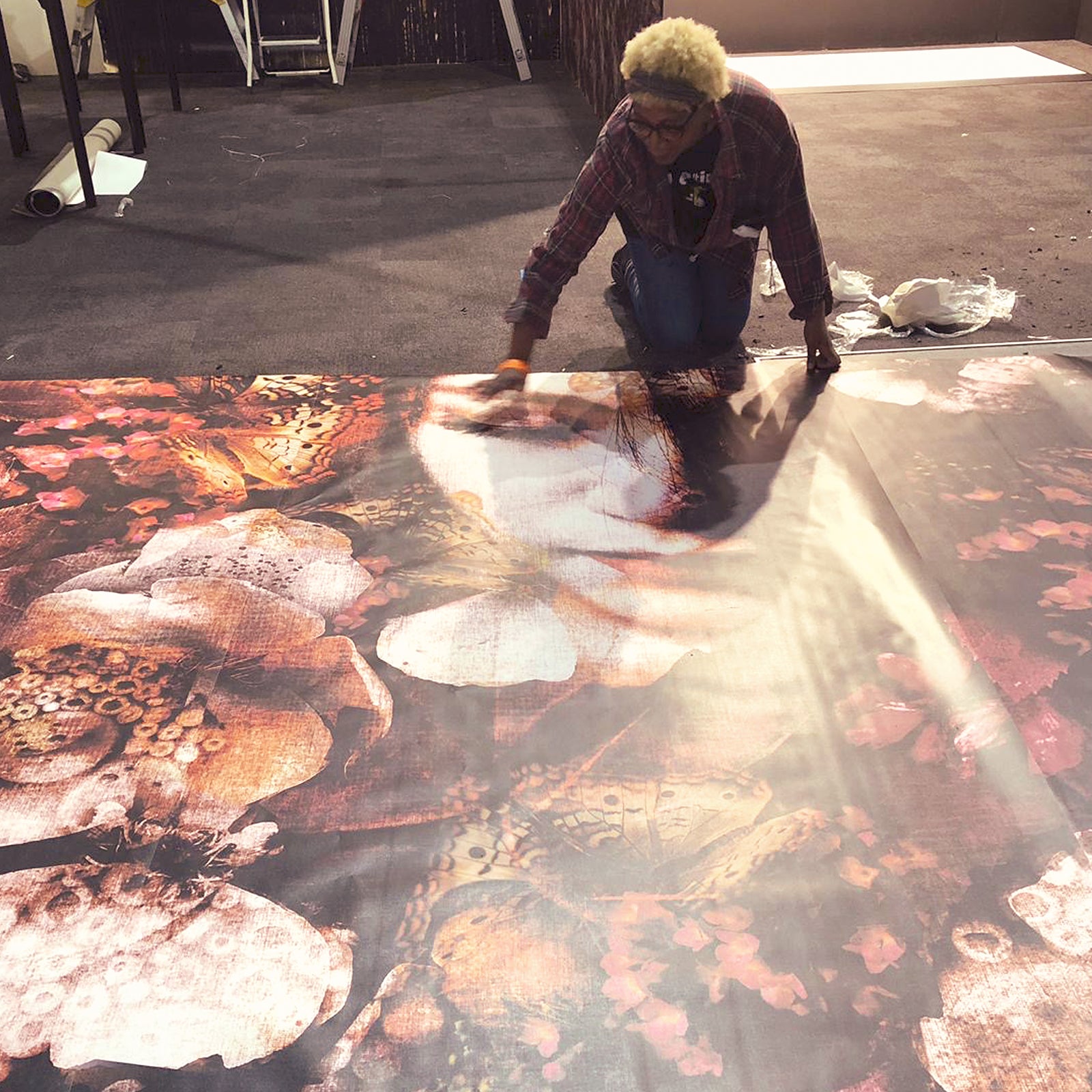 Annette Taylor-Anderson kneeling on he floor looking at Butterfly Joe mural design by ATADesigns in exhibition hall.