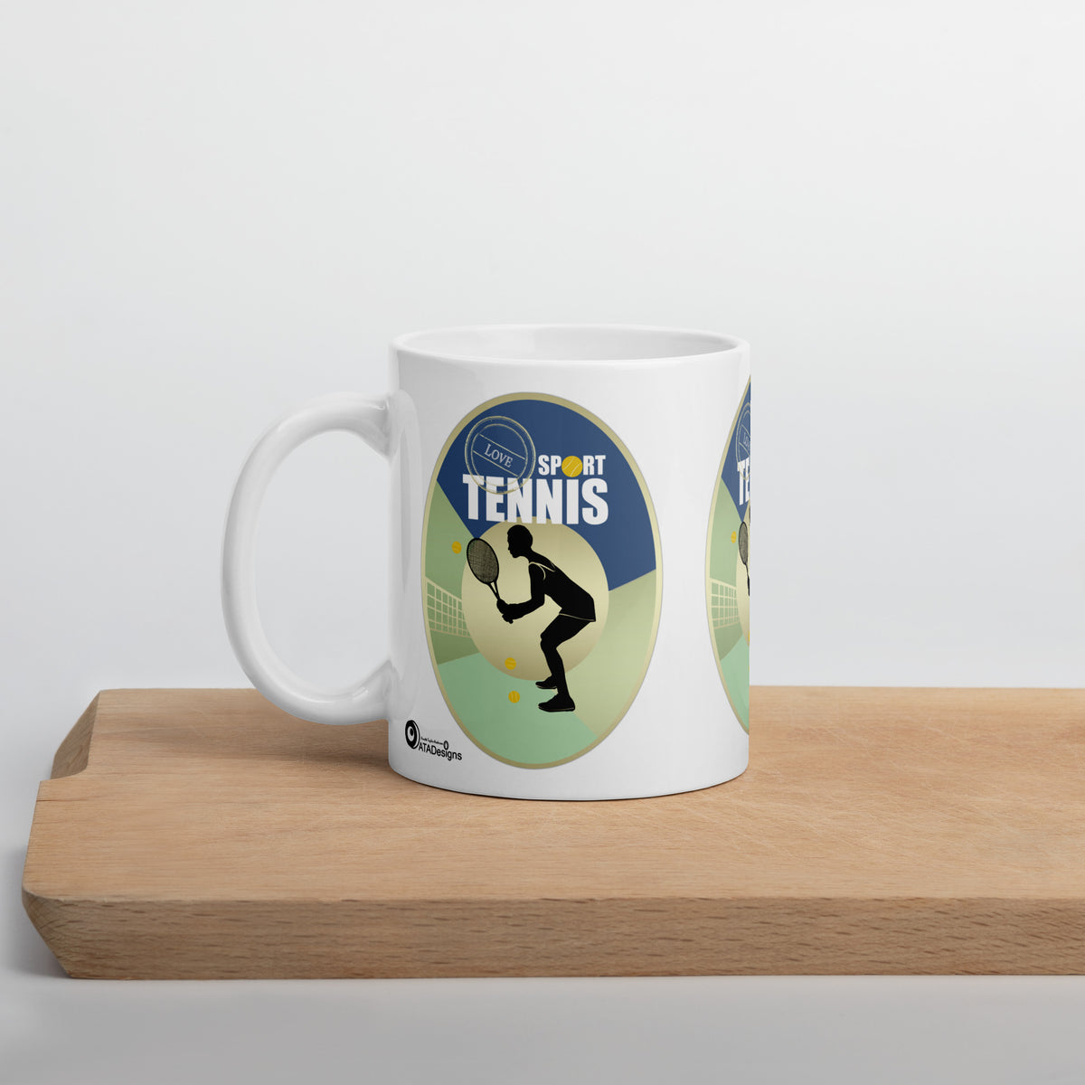 White Tennis Sport mug with a black tennis-player silhouette and blue and green artwork, displayed on a wooden board.